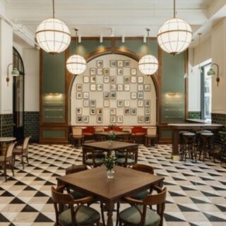Cafe interior with a black-and-white diamond-checkered floor, round pendant lights, and a wall gallery in an arched alcove.