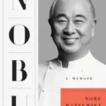 Book cover showing a black-and-white photo of Nobu Matsuhisa smiling on a gray background, with vertical 'NOBU' letters on the left and an orange rectangle containing 'NOBU MATSUSHISA' beneath a small 'A MEMOIR' subtitle.