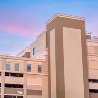 Modern multi-level parking garage with a tall central beige tower against a pink-blue sunset sky.