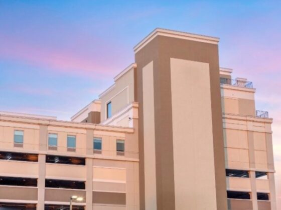 Modern multi-level parking garage with a tall central beige tower against a pink-blue sunset sky.