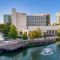 Hilton hotel complex along a river with a pedestrian boardwalk and fountain in the water ahead.