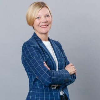 Professional woman with short blonde hair in a blue checkered blazer, arms crossed, smiling at the camera.