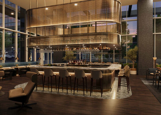 Interior of a contemporary hotel bar with a curved marble counter, beige bar stools, and a large metal mesh circular chandelier overhead, near floor-to-ceiling windows at dusk.