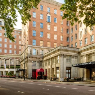 Brick hotel building with a grand stone entrance and a sign reading BALLROOM on a tree-lined city street.