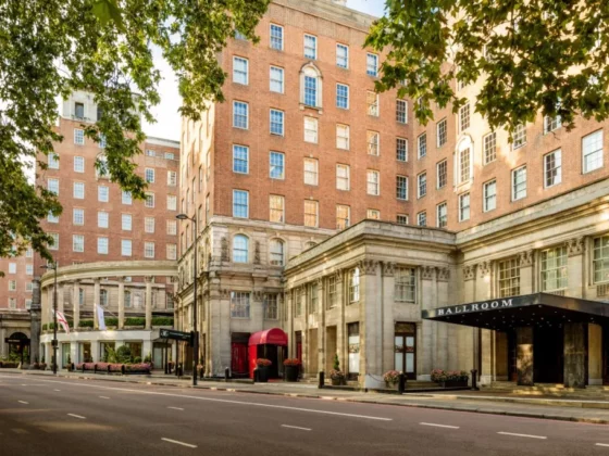 Brick hotel building with a grand stone entrance and a sign reading BALLROOM on a tree-lined city street.