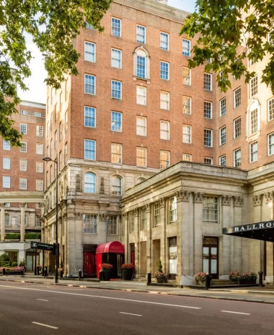 Brick hotel building with a grand stone entrance and a sign reading BALLROOM on a tree-lined city street.