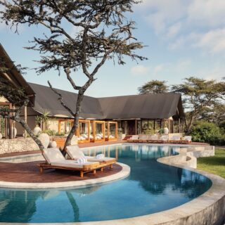 Luxurious resort pool curving around a wooden deck with lounge chairs under a shaded pavilion.