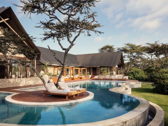 Luxurious resort pool curving around a wooden deck with lounge chairs under a shaded pavilion.