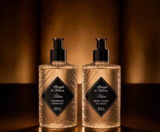 Two amber bottles with black diamond labels sit on a warm-lit shelf, labeled shampoo and body wash.