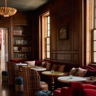 Luxurious wood-paneled lounge with red velvet seating, plaid chairs, round tables, and a chandelier grouping.