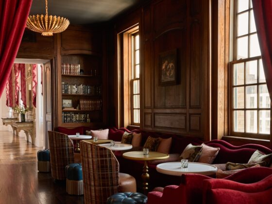 Luxurious wood-paneled lounge with red velvet seating, plaid chairs, round tables, and a chandelier grouping.