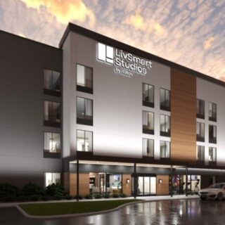 Exterior view of LivSmart Studios by Hilton, a modern four-story hotel at dusk with lit windows and a covered entrance.