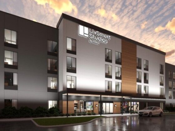 Exterior view of LivSmart Studios by Hilton, a modern four-story hotel at dusk with lit windows and a covered entrance.