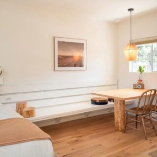 Bright minimalist room with a white bed, built-in bench, and a wooden table with two chairs near a window.