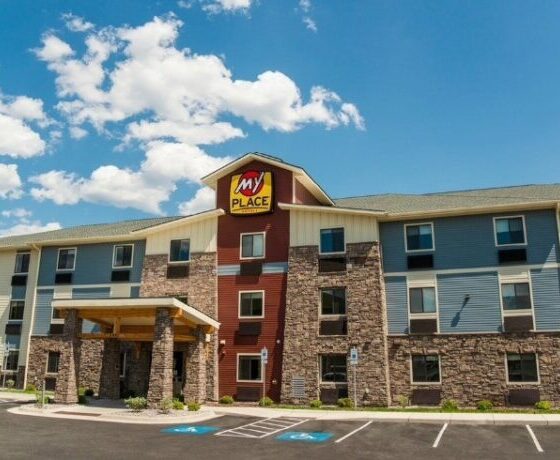 Exterior view of a My Place hotel with stone columns, blue siding, and a covered entry on a sunny day