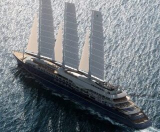 Aerial view of a large luxury sailing yacht with four masts sailing on deep blue ocean.