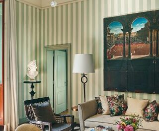 Living room with green striped walls, a beige sofa with colorful cushions, and large arched artwork above a coffee table.