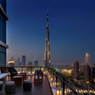 Rooftop terrace with seating and glowing lanterns overlooking Dubai skyline and the Burj Khalifa at dusk.