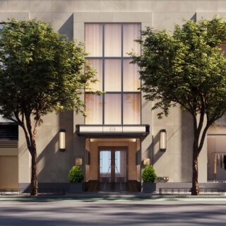 Modern building façade with large central glass doors framed by two trees and beige stone exterior