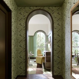 Arched doorway opening into a sunlit living room with a yellow armchair, green curtains, and a striped rug in view.