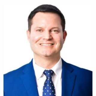 Smiling man in a blue suit, white shirt, and blue polka-dot tie.