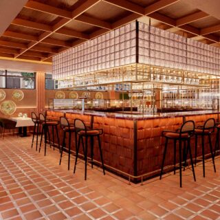 Luxurious orange-toned bar interior with a suspended glass rack, illuminated counter, and stools beneath decorative plates on the wall.