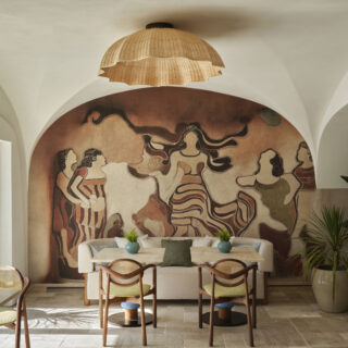 Dining area with a large curved mural mural of people, beige sofa, and wicker pendant lamp overhead.