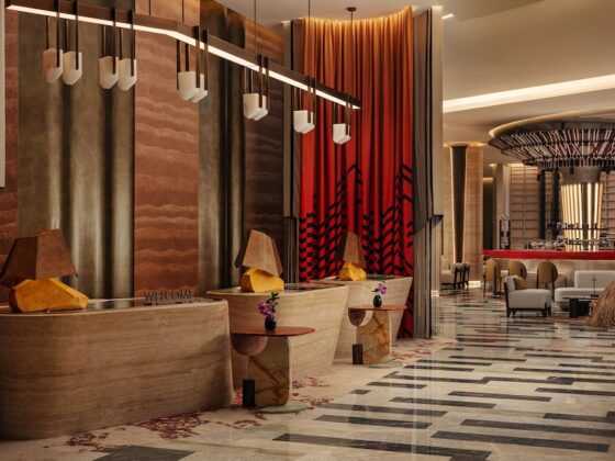 Hotel reception area with curved stone desk, warm pendant lights, and red drapes in a stylish lobby.