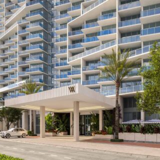 Modern glass-clad apartment building with multiple balconies and a covered entrance.
