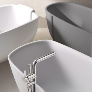Three minimalist freestanding bathtubs in a bright bathroom, white and gray, with a chrome faucet in the foreground and a towel on one tub.