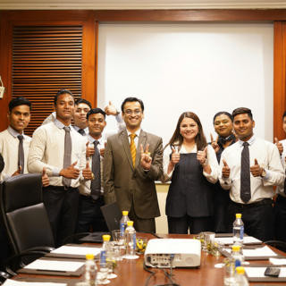 Group of professionals in a conference room posing for a photo, many giving thumbs up and smiling at the camera.
