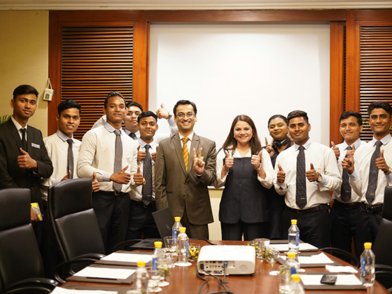 Group of professionals in a conference room posing for a photo, many giving thumbs up and smiling at the camera.