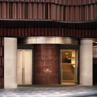 Mandarin Oriental hotel entrance with curved red-tiled wall, large glass doors, and a lit lobby plant visible inside.