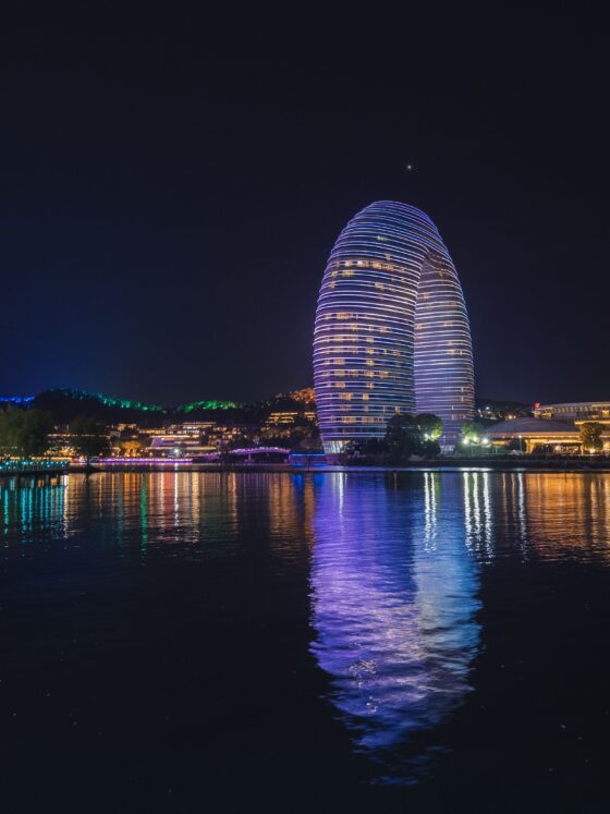 Nighttime city skyline with two glowing oval towers wrapped in blue lights by a river, reflections in the water.