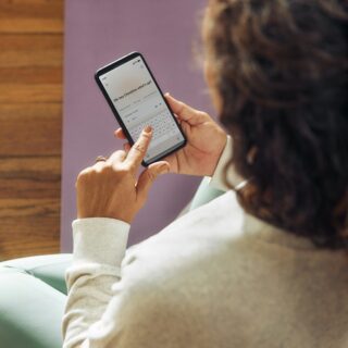 Person seen from behind holding a smartphone that displays a chat message reading 'Oh hey Christina what's up?'
