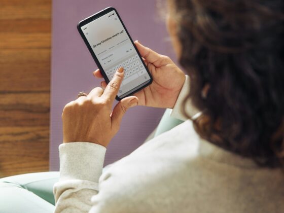 Person seen from behind holding a smartphone that displays a chat message reading 'Oh hey Christina what's up?'