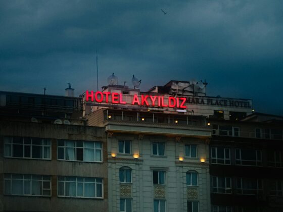 Red neon sign reading 'HOTEL AKYILDIZ' atop a multi-story building under a cloudy, evening sky at dusk.