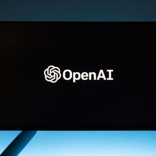 OpenAI logo illuminated on a dark screen mounted outdoors against a blue sky backdrop
