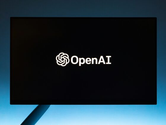 OpenAI logo illuminated on a dark screen mounted outdoors against a blue sky backdrop