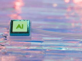 Circuit module with a green AI label mounted on a blue housing, set against a pastel sky background.
