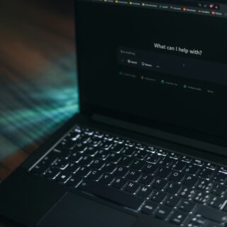 Laptop screen displaying a dark help panel with the prompt 'What can I help with?' and a search field nearby.