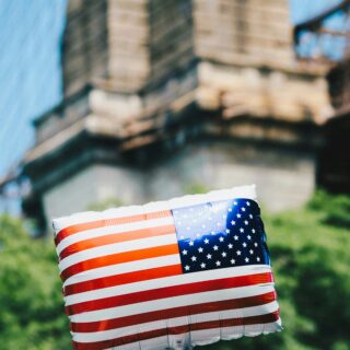 American flag–themed balloon floating outdoors with red, white, and blue stripes; green trees in the background.