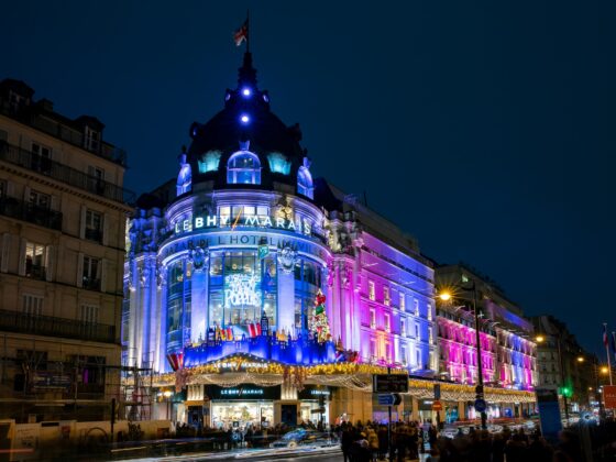 Nighttime facade of Le BHV Marais department store in Paris, illuminated in blue and pink; crowds at street level and festive lights above the entrance
