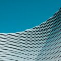 Blue sky above a curved, woven metal facade of a modern building.