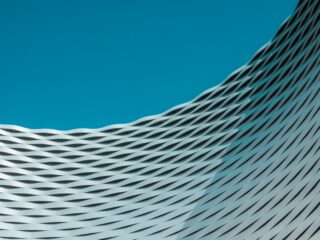 Blue sky above a curved, woven metal facade of a modern building.
