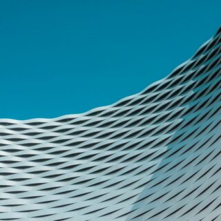 Blue sky above a curved, woven metal facade of a modern building.