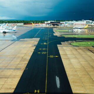 Wide airport runway and taxiways with planes at gates beneath a dark stormy blue sky and wet tarmac.