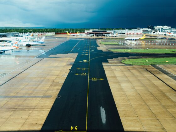 Wide airport runway and taxiways with planes at gates beneath a dark stormy blue sky and wet tarmac.