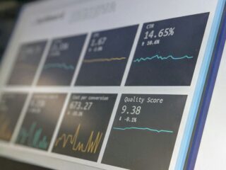 Blurred close-up of a data dashboard with line charts and numeric metrics, including a 'Quality Score' value visible on the screen.
