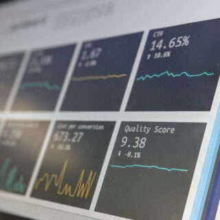 Blurred close-up of a data dashboard with line charts and numeric metrics, including a 'Quality Score' value visible on the screen.